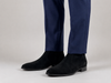 Premium black suede Chelsea boots for men with sleek almond toe and elastic side panels worn with navy formal trousers on a minimalist studio background.