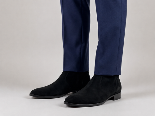 Premium black suede Chelsea boots for men with sleek almond toe and elastic side panels worn with navy formal trousers on a minimalist studio background.