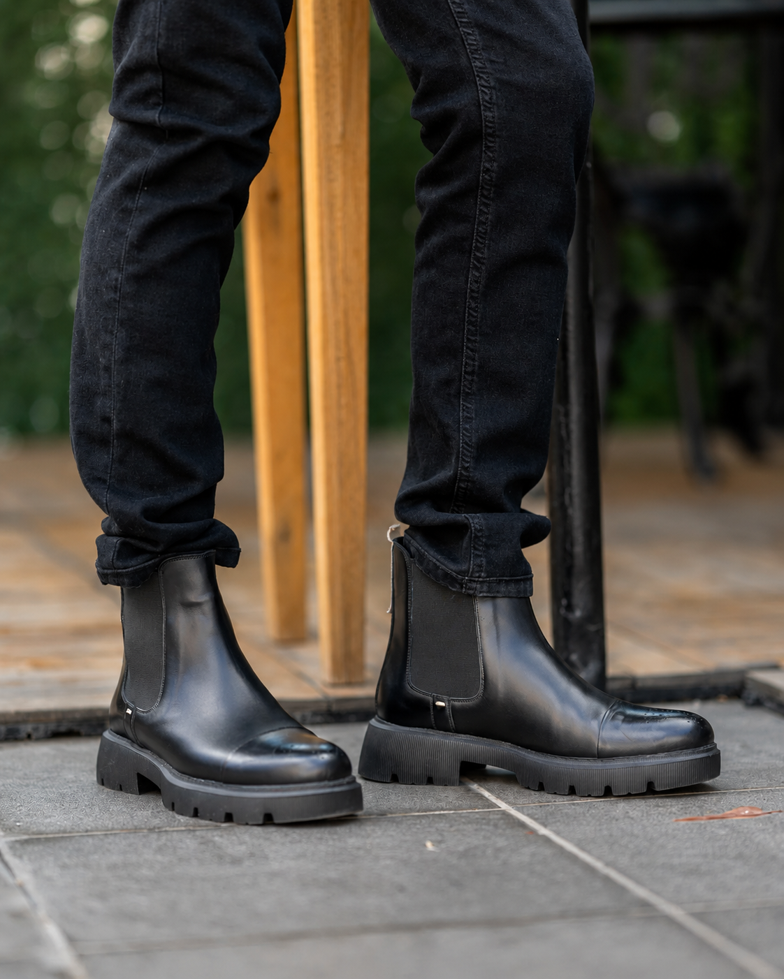 Black leather boots worn with black pants on a stone surface.