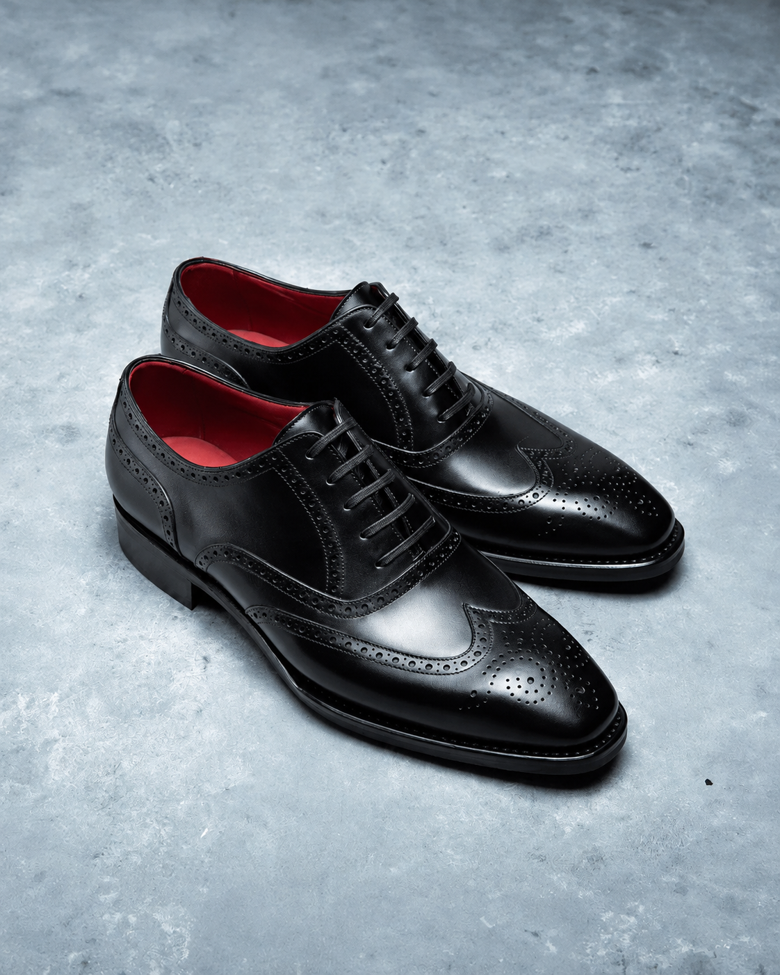 Pair of black dress shoes with red lining on a gray textured surface