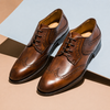 Pair of brown leather dress shoes on a light blue and beige background