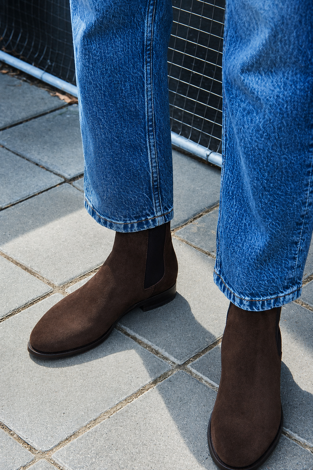 Brown suede ankle boots worn with blue jeans on a stone pavement.