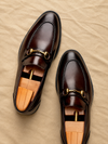 Pair of brown leather loafers with gold buckles on a beige surface