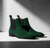 Pair of green suede Chelsea boots on a light gray background