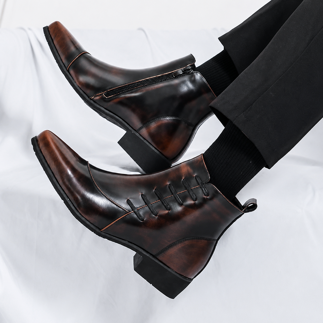 Men's Milano Burnished Leather Chelsea Boots in a rich dark brown patina finish, featuring a sleek square toe, side zipper, and modern lace detailing, styled with black tailored trousers in a premium studio setting.
