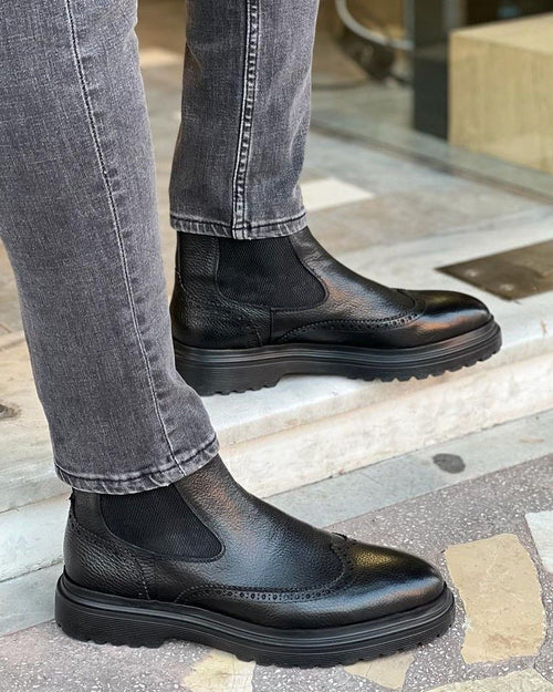 Black leather Chelsea boots worn with gray jeans on a sidewalk.
