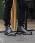 Black leather boots worn with black pants on a stone pavement.