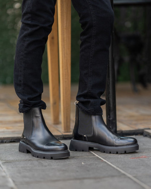 Black leather boots worn with black pants on a stone pavement.