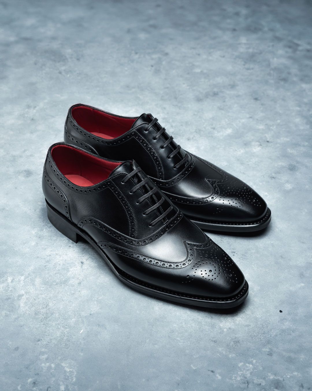 Black leather dress shoes with red lining on a gray surface