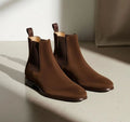 Pair of brown Chelsea boots on a light surface with a neutral background