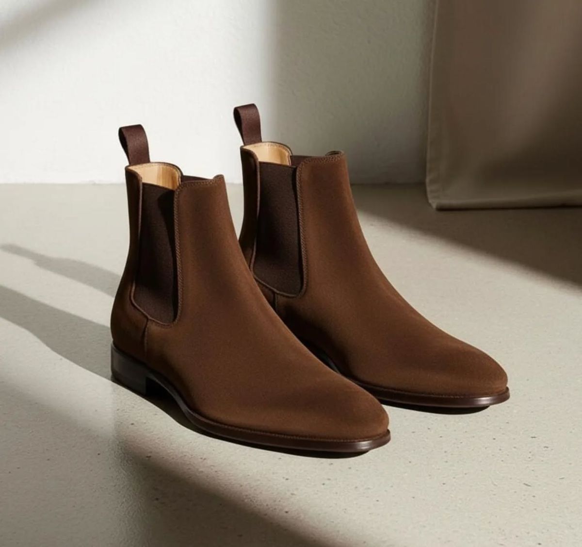 Pair of brown Chelsea boots on a light surface with a neutral background