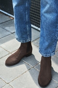 Brown suede boots worn with blue jeans on a stone pavement.