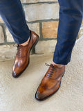 Brown dress shoes worn with blue checkered pants against a stone wall background