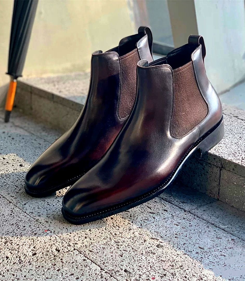 Pair of brown leather Chelsea boots on a concrete surface with a blurred background.