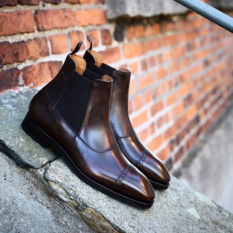 Pair of brown leather boots on a stone ledge with a brick wall background