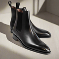 Pair of black leather Chelsea boots on a light wooden surface