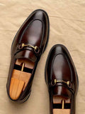 Pair of brown leather loafers with gold buckles on a beige surface