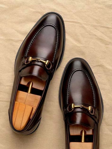 Pair of brown leather loafers with gold buckles on a beige surface