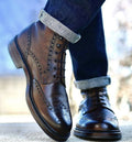 Brown leather brogue shoes worn with rolled-up jeans on a blurred outdoor background