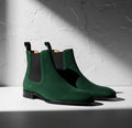 Green Chelsea boots on a white surface with a textured gray background