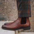 Brown woven Chelsea boots worn with plaid pants against a blurred background