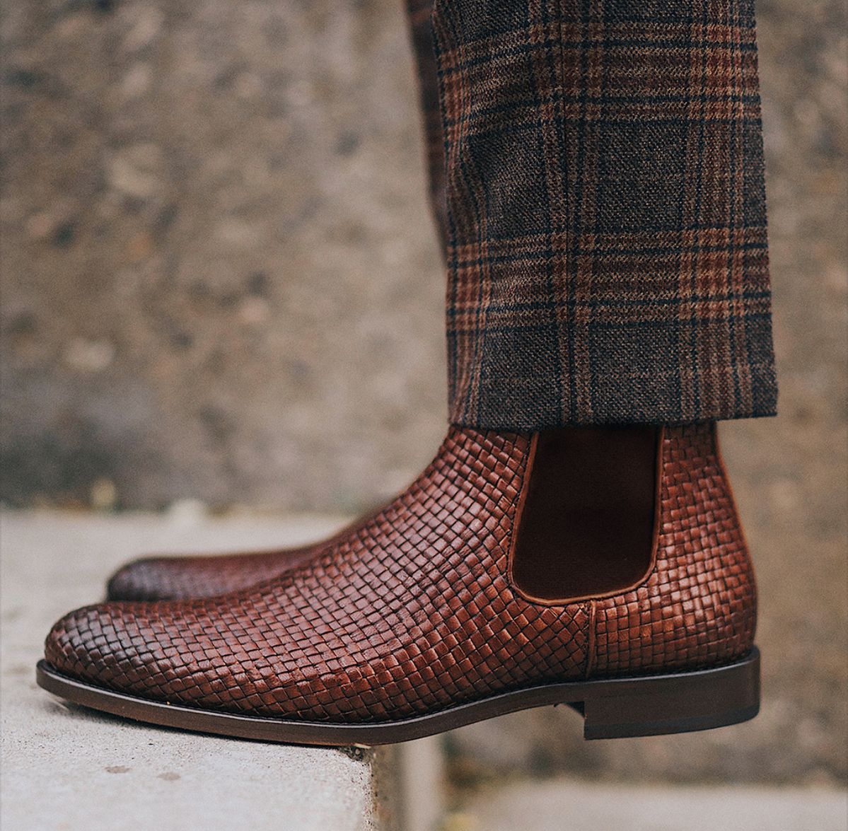 Brown woven Chelsea boots worn with plaid pants against a blurred background