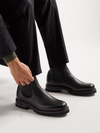Person wearing black leather boots on a light gray background