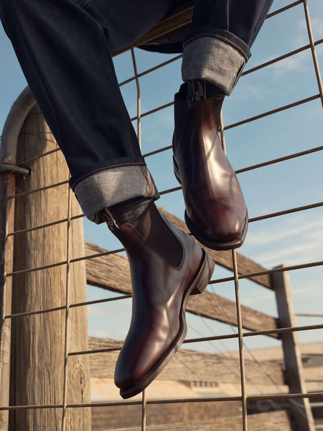 Person wearing brown leather shoes standing on a wire fence with a clear sky background