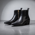 Pair of black leather boots with a gold zipper on a gray background