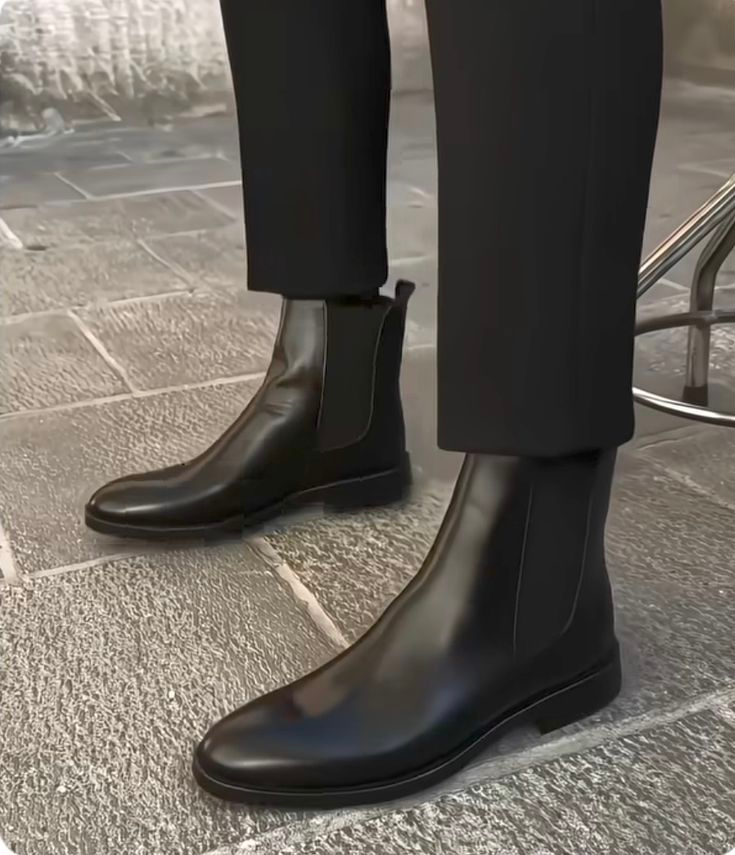 Black leather Chelsea boots worn with black pants on a stone pavement.