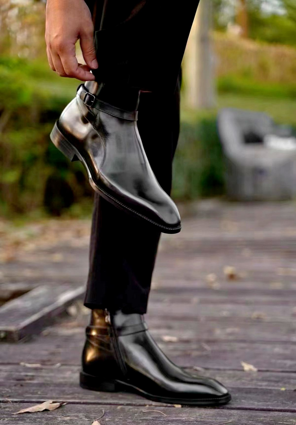 Person wearing black leather shoes on a wooden deck with blurred greenery in the background