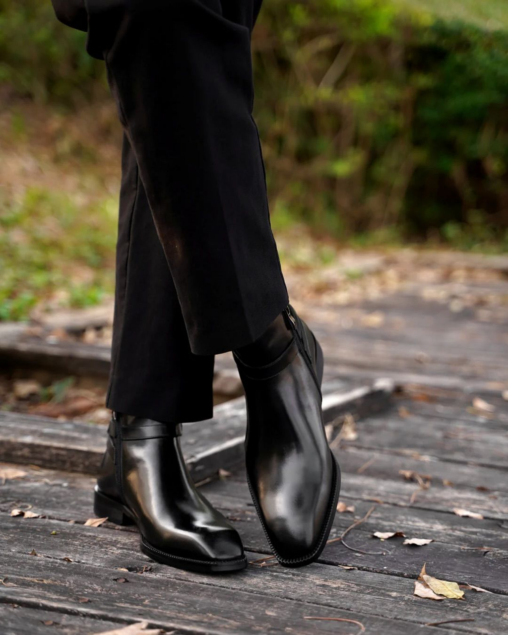 Black leather boots worn with black pants on a wooden floor.