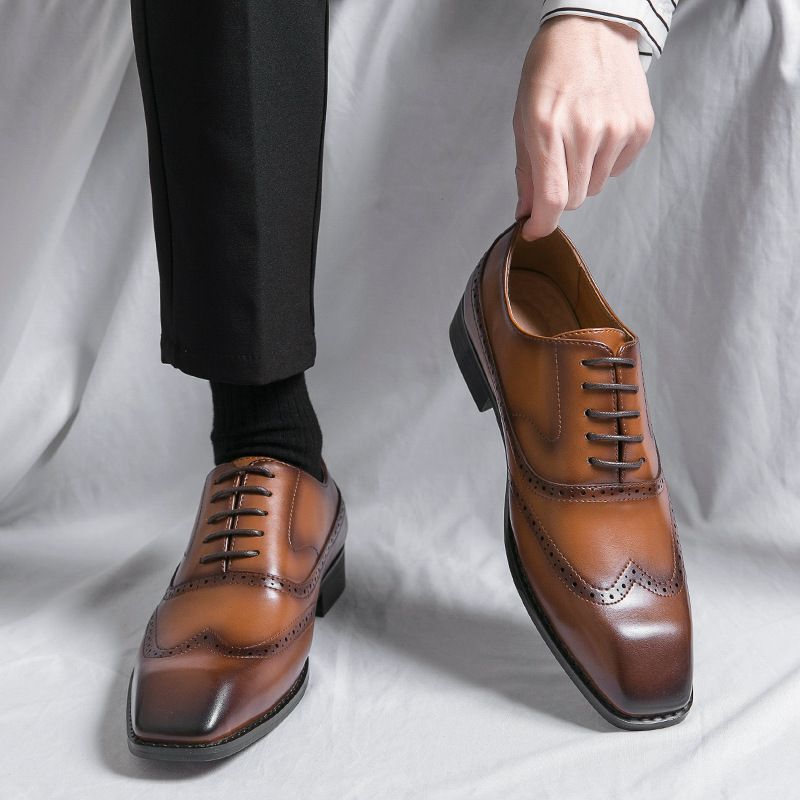 Brown dress shoes being held up against a white background