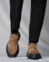 Men's Tuscany Tan Brogue Derby Shoes crafted from premium Italian leather with a chunky black lug sole, worn with black tailored trousers in a luxury studio setting.