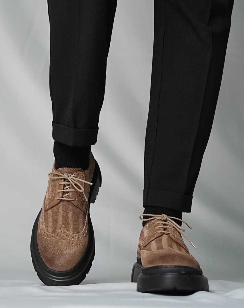 Brown suede shoes with black soles worn with black pants on a light gray background