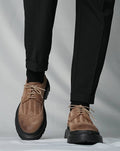 Brown suede shoes with black soles worn with black pants on a light gray background