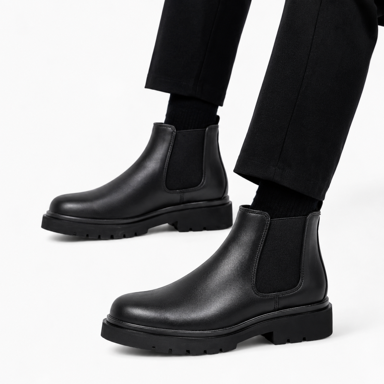 Black leather Chelsea boots worn with black pants on a white background