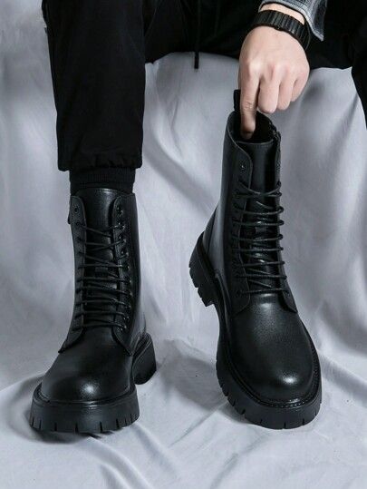 Person wearing black leather boots on a light gray background