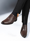Brown dress shoes worn with black pants on a light gray background