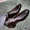 Brown leather shoes worn with gray pants on a textured pavement.