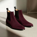 Pair of maroon Chelsea boots on a light surface with a neutral background