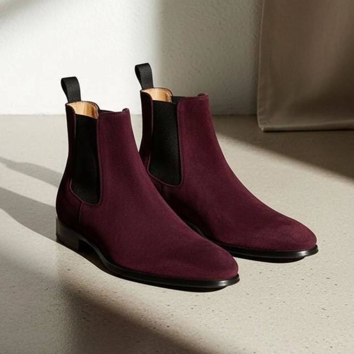 Pair of maroon Chelsea boots on a light surface with a neutral background